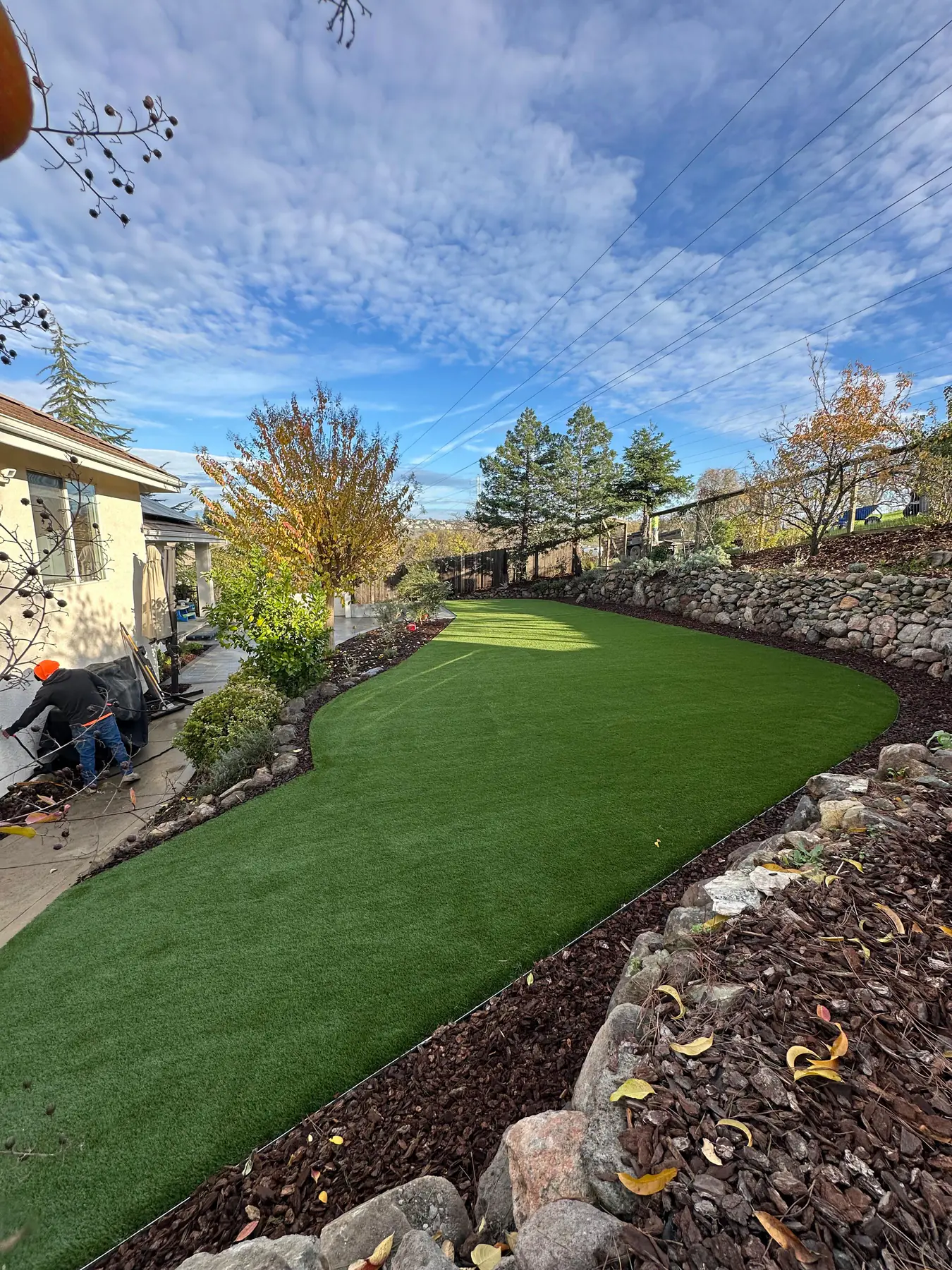 Bright sunlit front yard with white fence and lush green artificial turf, airy open environment, well-lit daytime scene